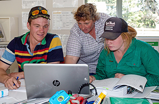image of two students looking at laptop with teacher